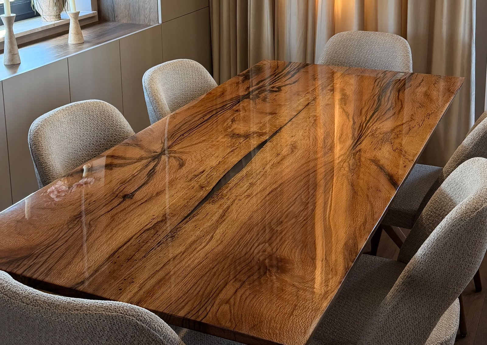 Solid oak dining table with dark mineral streaks, a resin-filled natural crack and a high-gloss epoxy top, surrounded by beige bouclé chairs in a warm dining room