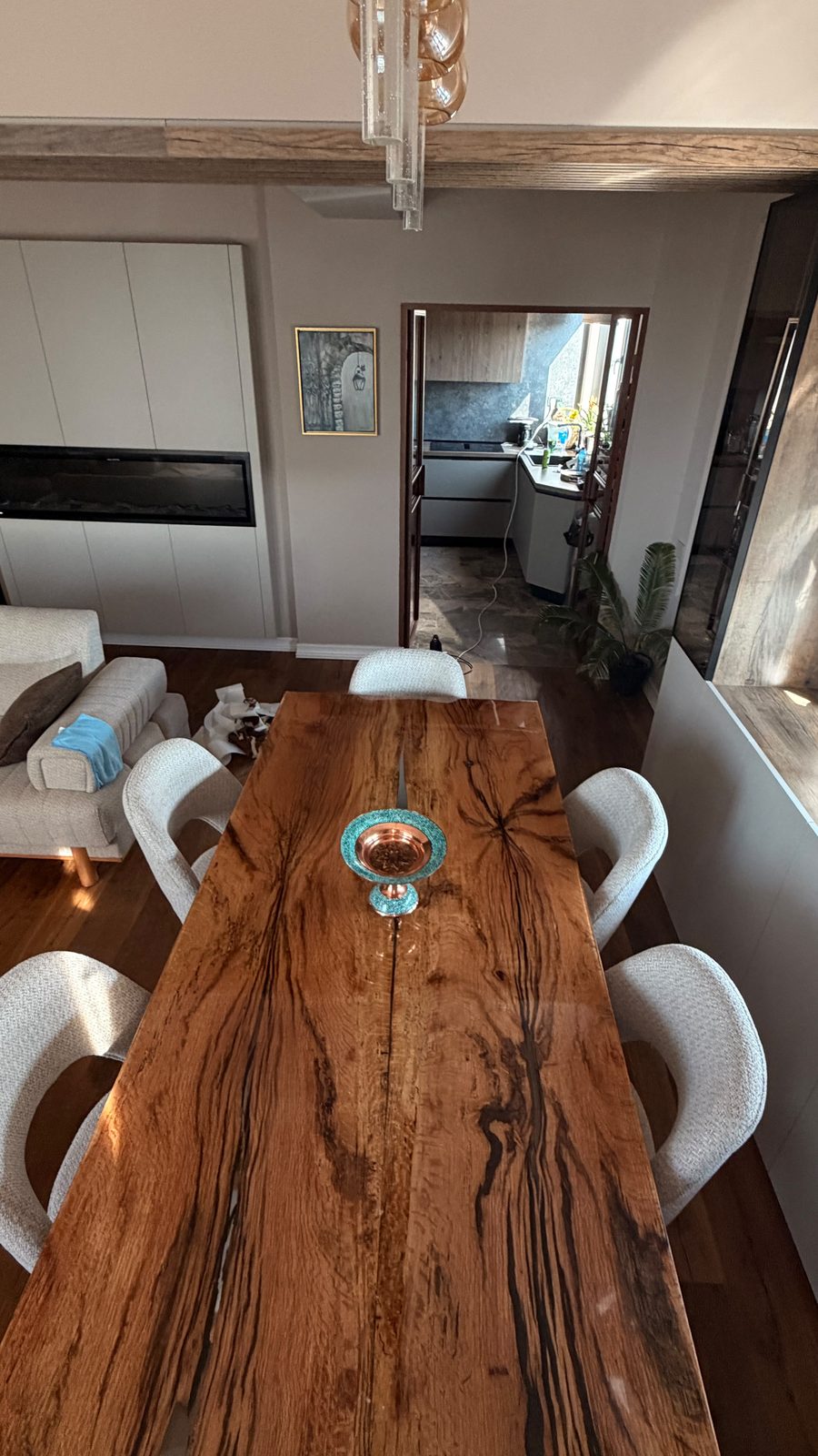 Top-down view of the full oak and resin dining table in an open-plan living space with white bouclé chairs